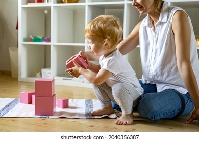 Young mother and little baby assembling pink cube Maria Montessori ecological materials method early development. Confident family constructing toy tower use self educational game at home