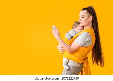 Young Mother With Little Baby In Sling With Mobile Phone On Color Background