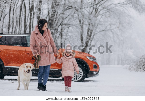 Young mother with little daughter and pet walking in\
a winter park by the car