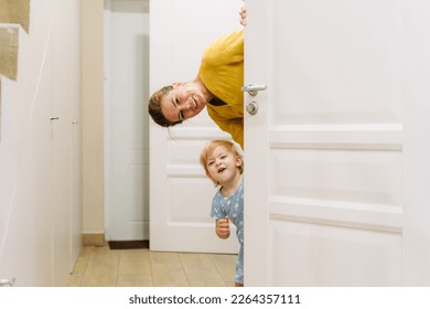 A young mother and little daughter play hide-and-seek behind the door of the house.