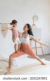 Young Mother With Little Daughter Practice Yoga Home. Warrior Pose.