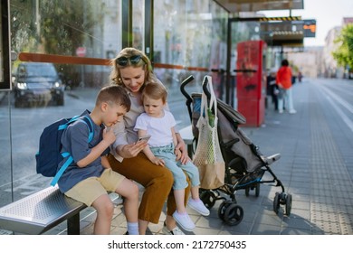 Young mother with little kids waiting on bus stop in city, scrolling on mobile phone. - Powered by Shutterstock