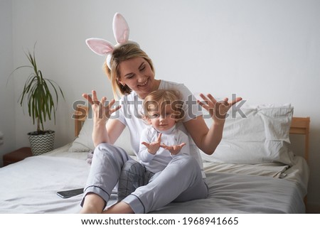 young mother and little son in rabbit ears have fun at home on the bed