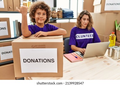 Young Mother With Little Son Wearing Volunteer T Shirt At Donations Stand Pointing Thumb Up To The Side Smiling Happy With Open Mouth 