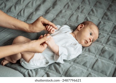 Young mother is massaging her newborn baby's feet on the bed, shown in a close-up of hands and body, with warm colors, in an indoor environment with natural light. - Powered by Shutterstock