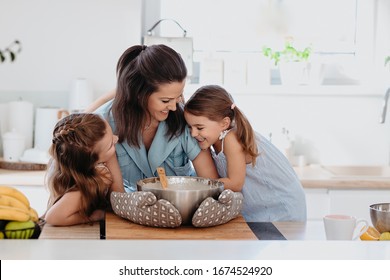 Young Mother Or A Nanny With Little Kids Is Cooking In The White Kitchen And Laughing Having Fun. Making Pancakes Together And Smiling.