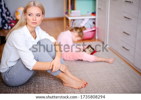 Young mother is nervous and sad at home on the floor, the child watches cartoons on the tablet and plays, naughty child, family concept.
