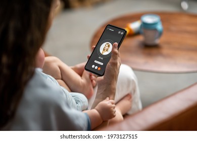 Young Mother With Newborn Kid Making Video Call To A Doctor Using Phone At Home. Concept Of Telemedicine And Support Parents Counseling Online. 