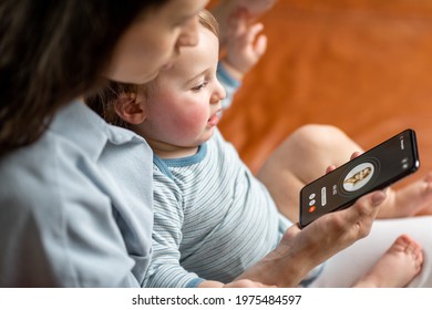 Young Mother With Newborn Kid Making Video Call To A Doctor Using Phone At Home. Concept Of Telemedicine And Support Parents Counseling Online. 