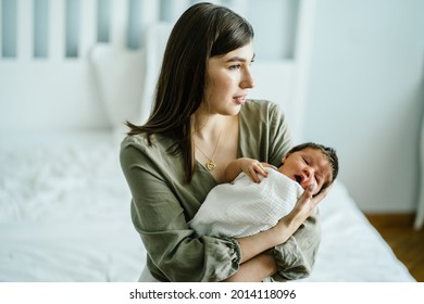 Young mother nursing and caressing her little sweet newborn bay at bedroom at home. Cute infant kid calming on mother's hands.