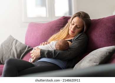 Young mother on the sofa breastfeeding her newborn baby
