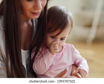 Young mother playing with her curious baby daughter sucking her thumb at home. Mom and baby girl looking at something interesting - Shutterstock ID 1395707102