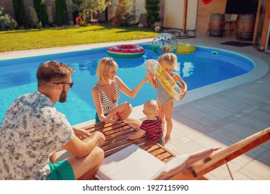 Young mother playing with little children by the swimming pool on a hot sunny summer day, little girl trying on swim ring while baby boy is eating watermelon - Powered by Shutterstock