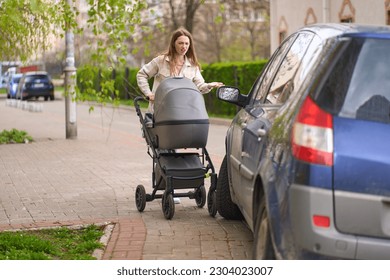 Young mother pushing stroller with her newborn child, feels outraged by an incorrectly parked car on a pedestrian sidewalk, blocking the passage of pedestrians walking down the street, with baby prams