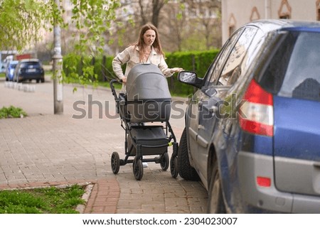 Young mother pushing stroller with her newborn child, feels outraged by an incorrectly parked car on a pedestrian sidewalk, blocking the passage of pedestrians walking down the street, with baby prams