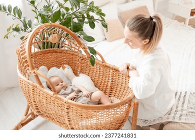 a young mother puts her little newborn baby to sleep in a wicker cradle in the bedroom and we sing him a song, the love and care of a mother for a child, mom and baby. - Powered by Shutterstock