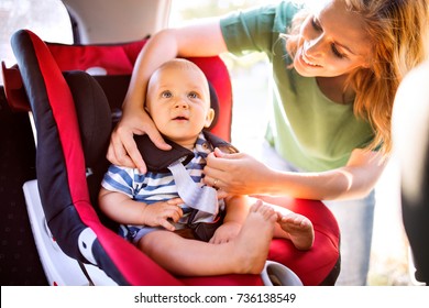 Young Mother Putting Baby Boy In The Car Seat.