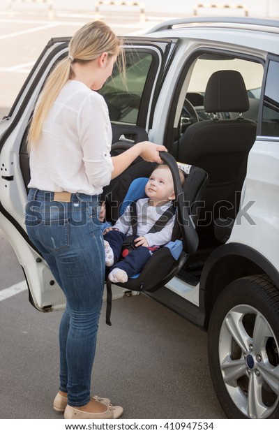 Young mother putting car seat with her baby boy in\
the car