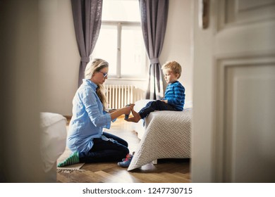 A young mother putting socks on toddler son inside in a bedroom. - Powered by Shutterstock