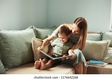 Young Mother, Read A Book To Her Child, Boy In The Living Room Of Their Home, Rays Of Sun Going Through The Window