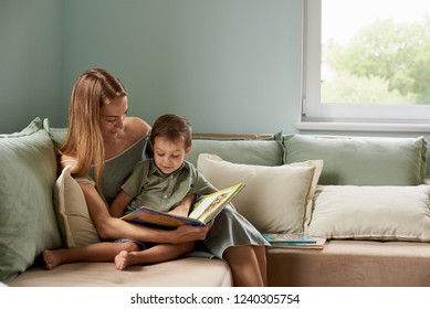 Young Mother, Read A Book To Her Child, Boy In The Living Room Of Their Home, Rays Of Sun Going Through The Window