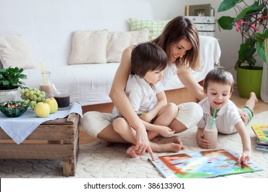 Young Mother, Read A Book To Her Two Children, Boys, In The Living Room, Eating Fruits And Drinking Smoothie, Mothers Day Concept
