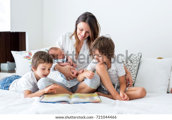 Young mother, read a book to her\
three children, boys, in the bedroom, mothers day\
concept