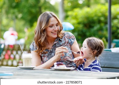 Young Mother Relaxing Together With Her Little Child, Adorable Toddler Girl, In Summer Outdoors Cafe Drinking Coffee And Eating Muffin Or Cupcake. Selective Focus On Child.