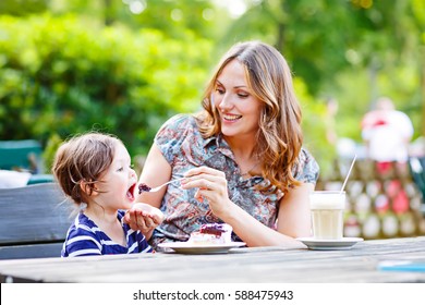 Young Mother Relaxing Together With Her Little Child, Adorable Toddler Girl, In Summer Outdoors Cafe Drinking Coffee And Eating Muffin Or Cupcke. Family In Love. Kid An Beautiful Woman.