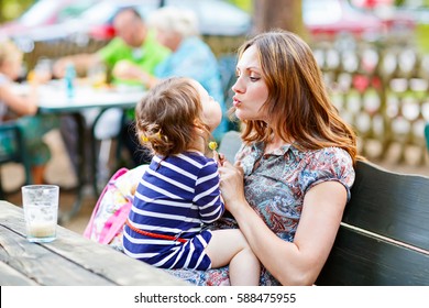 Young Mother Relaxing Together With Her Little Child, Adorable Toddler Girl, In Summer Outdoors Cafe Waiting For Coffe. Happy Family Hugging, Beautiful Woman And Tiny Cute Kid.