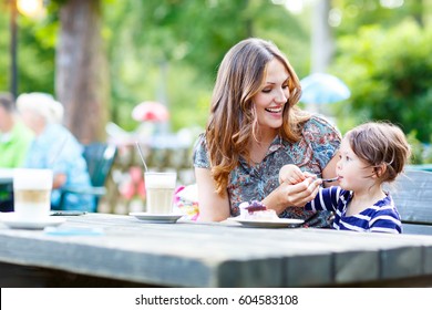 Young Mother Relaxing Together With Her Little Child, Adorable Toddler Girl, In Summer Outdoors Cafe Drinking Coffee And Eating Muffin Or Cupcke. Family In Love. Kid An Beautiful Woman.