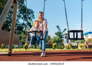 A young mother rides a child on a swing, on the playground. Outdoor. The concept of the Children's Day. - Powered by Shutterstock