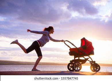 Young Mother Is Running To Stroller With A Baby At Sunset