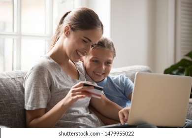 Young mother and schoolchild daughter sitting on sofa in living room look at notebook screen use credit card paying money distantly buying in internet making secure payment online via ebanking service
