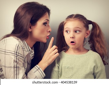 Madre joven mostrando el dedo el signo del silencio a su sorprendente hija y hablando "no hables al padre". Retrato de concepto vintage de cierre tachado