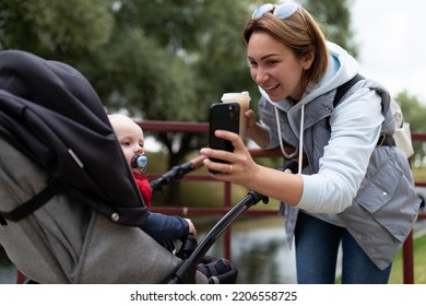 Young Mother Shows A Child In A Stroller Cartoon On The Phone