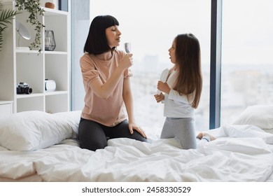 Young mother sings with her little adorable daughter using combs instead of microphones while sitting on bed. Happy Caucasian family having fun on a weekend morning. - Powered by Shutterstock