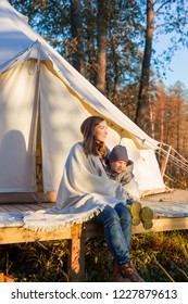 Young mother sitting with her kid near traditional canvas bell tent outdoor at sunset
