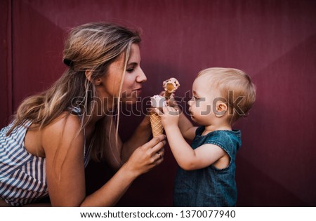 Young mother with small toddler girl outdoors in summer, eating ice cream.