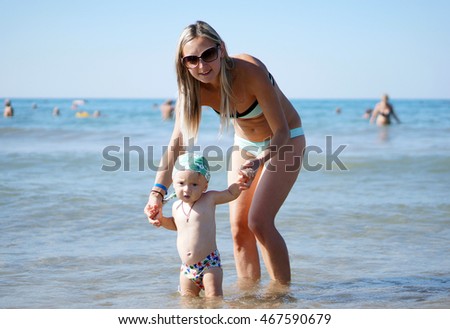Young mother smiling baby boy son in green baseball cap playing in the sea in the day time. Positive human emotions, feelings, joy. Funny cute child making vacations and enjoying summer.       