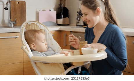 Young mother smiling at her baby son sitting in highchair at kitchen. Concept of parenting, healthy nutrition and baby care - Shutterstock ID 2311763563