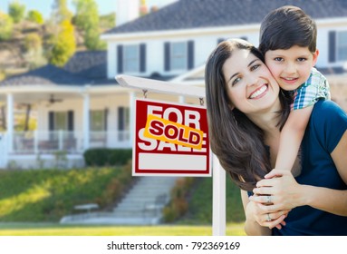 Young Mother and Son In Front of Sold For Sale Real Estate Sign and House.
