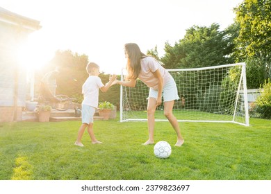 Young mother and son giving five during soccer game in the garden. Happy family playing football, having fun together. Fun Playing Games in Backyard Lawn on Sunny Summer Day. Motherhood, childhood - Powered by Shutterstock