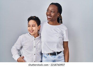 Young Mother And Son Standing Together Over White Background Looking Away To Side With Smile On Face, Natural Expression. Laughing Confident. 