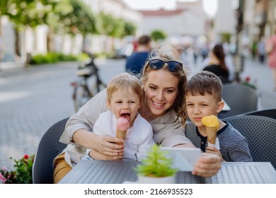 Young mother taking selfie with her kids eating ice-cream in cafe outdoors in street in summer. - Powered by Shutterstock