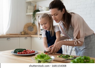 Young mother teach little preschooler daughter chop vegetables preparing salad for lunch together, loving mom and small girl child cooking dinner together, kid helping mommy with food preparation - Powered by Shutterstock