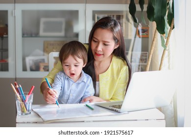 Young mother teaching her kid learning or painting at home. Happy mixed race Asian-German family woman and son homeschooling with computer laptop.