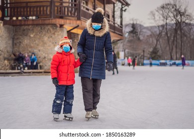 Young Mother Teaching Her Little Son Ice Skating At Outdoor Skating Rink. Family Wearing A Medical Mask During COVID-19 Coronavirus Enjoy Winter On Ice-rink Outdoors