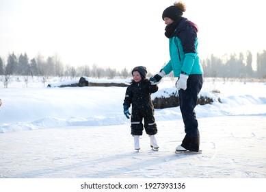 Young Mother Teaching Her Little Son Ice Skating At Outdoor Skating Rink. Family Enjoy Winter On Ice-rink Outdoors