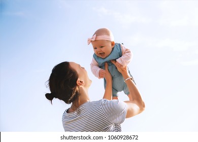 Young mother throws up baby in the sky, summer outdoors. Happy mom and cute smiling baby girl. Positive human emotions, feelings, natural lifestyles. Family background. - Powered by Shutterstock
